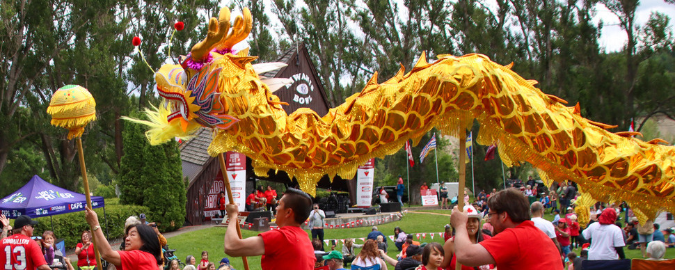 Three people dressed in red shirts are controlling a large golden dragon puppet as they navigate through a crowd on a grass field