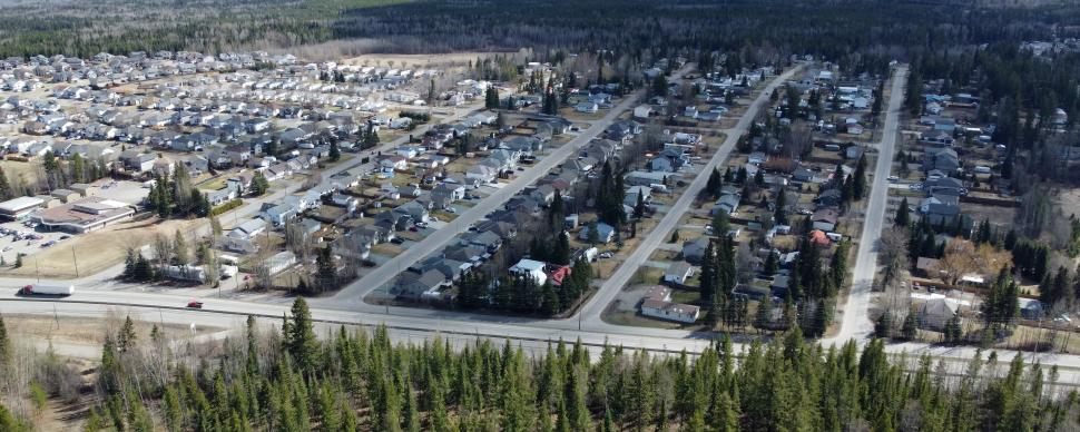 An aerial view of a forested area and city subdivision separated by a narrow highway