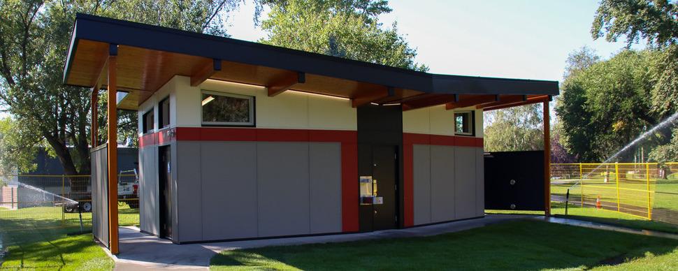 Exterior of a washroom facility in a park, surrounded by green grass and trees.