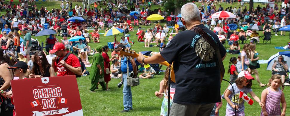 A musician with guitar on an outdoor stage in front of a large crowd.