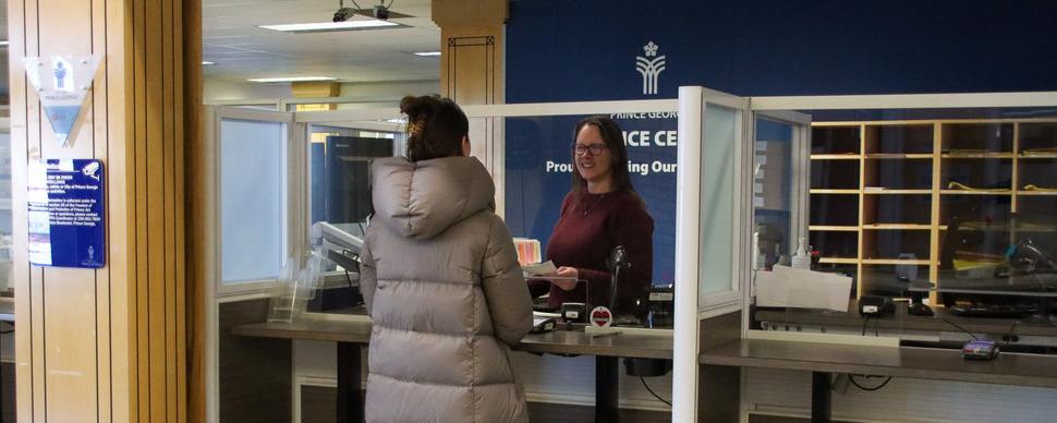 A smiling staff member is helping at resident at a Service Centre desk in City Hall