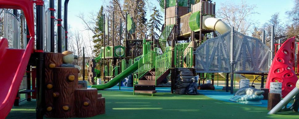 Playground equipment including large climbing structures, slides, and a reclining Mr PG sculpture